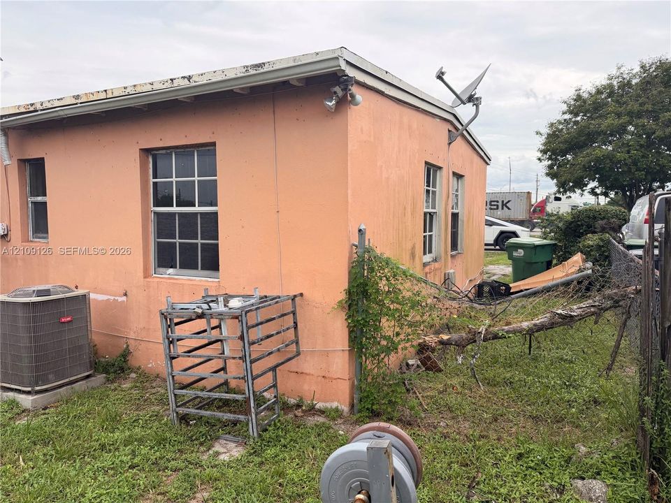 Stucco exterior featuring multiple grid-pane windows, a wall-mounted floodlight, and an external HVAC unit