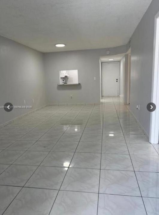 Neutral-toned interior space featuring light-colored ceramic tile flooring, flush-mount ceiling lighting, and a service pass-through window with a shelf