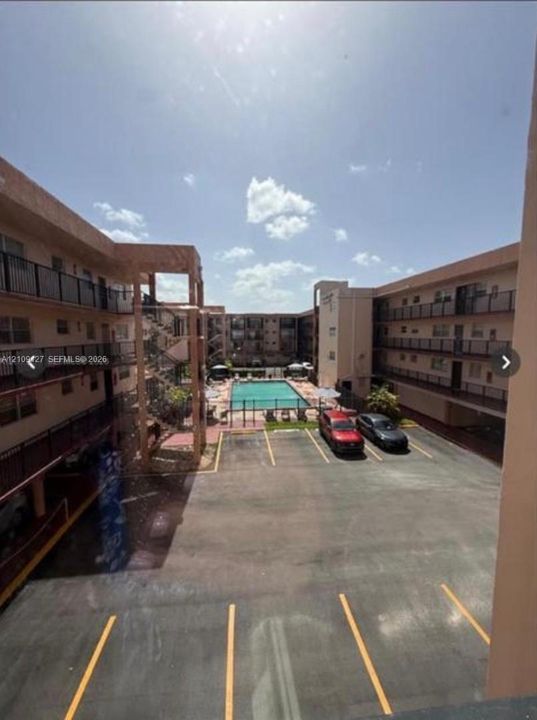 Exterior courtyard featuring a central swimming pool, paved surface parking, and multi-level buildings with metal railings