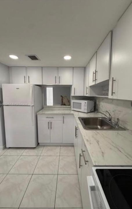 Kitchen featuring white cabinetry, stone-finish countertops, stainless steel sink, large-format tile flooring, and recessed lighting
