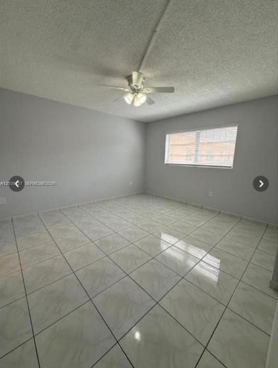 Interior space featuring large-format tile flooring, textured ceiling, central ceiling fan with integrated lighting, and a single-pane window