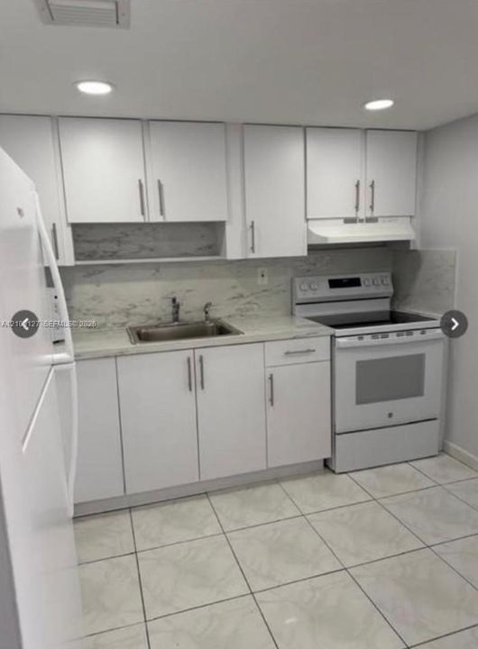 Kitchen featuring white cabinetry, stone-finish countertops, full-height backsplash, recessed ceiling lighting, and large-format tile flooring