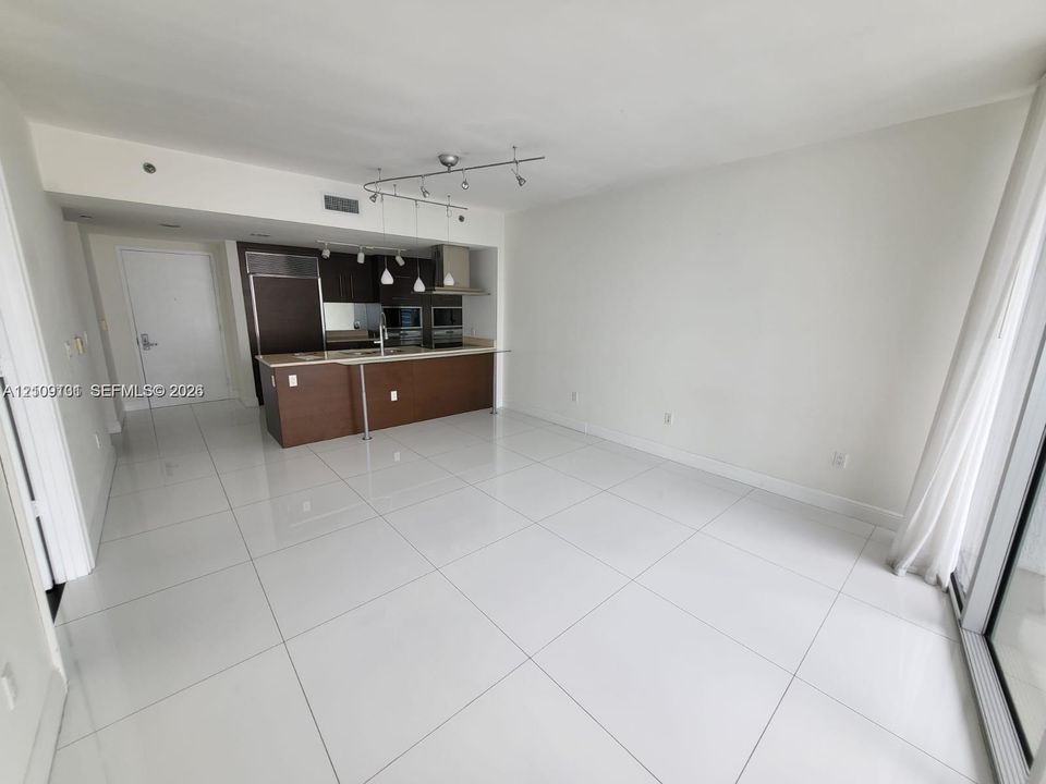Open-concept kitchen featuring dark wood-finish cabinetry, a breakfast bar with light-toned countertop, stainless steel built-in appliances, track lighting, and white tile flooring