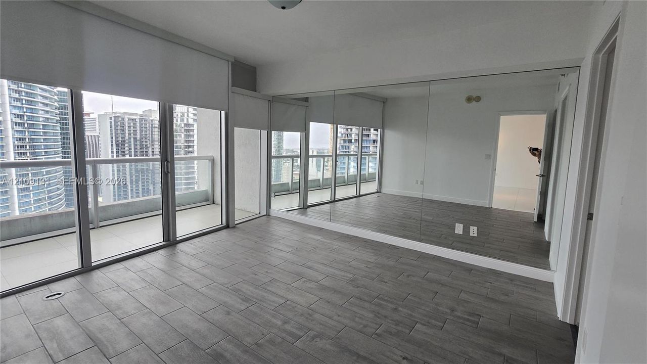 Living space featuring grey tile flooring, floor-to-ceiling mirrored wall, full-height windows with installed shades, and an exterior balcony