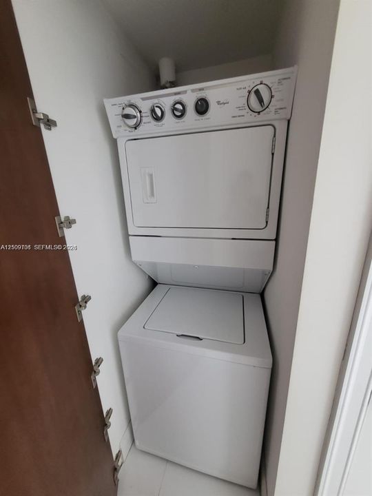 Stacked laundry unit featuring a white top-load washer and integrated dryer