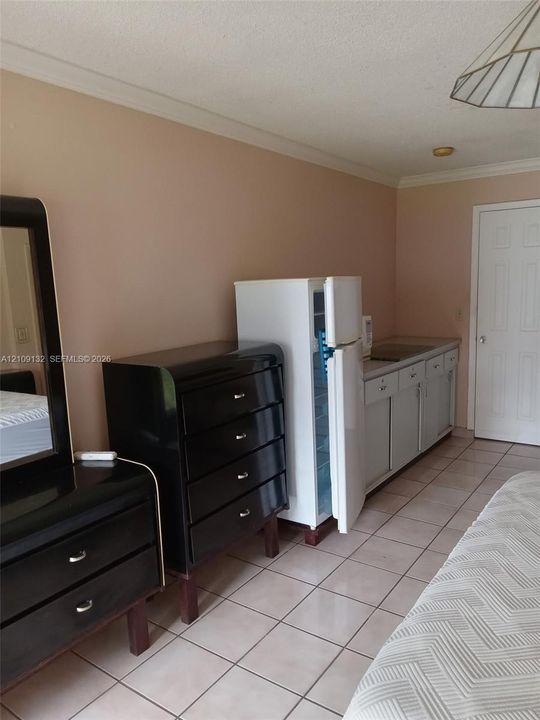 Kitchenette area featuring light-toned cabinetry, a compact refrigerator, a recessed sink, and tile flooring