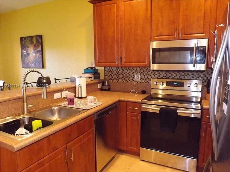 Kitchen featuring stained wood cabinetry, stainless steel appliances, a multi-tone tile backsplash, and a double-basin sink with a gooseneck faucet