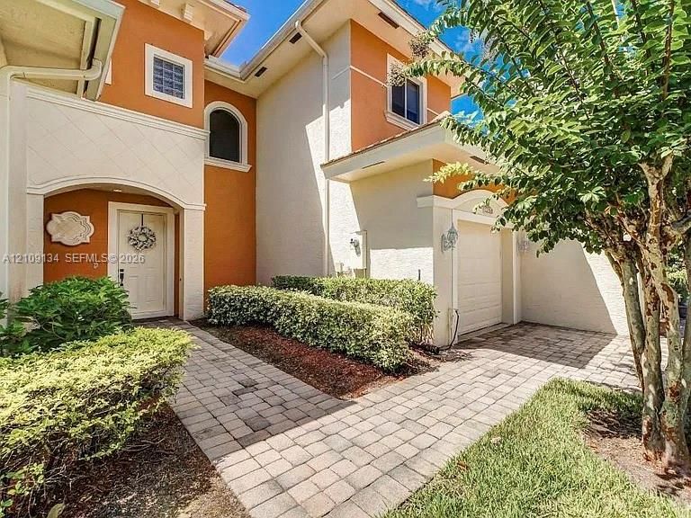 Stucco exterior featuring dual-tone facade, arched entryway, multi-paned windows, paver walkway, and attached one-car garage