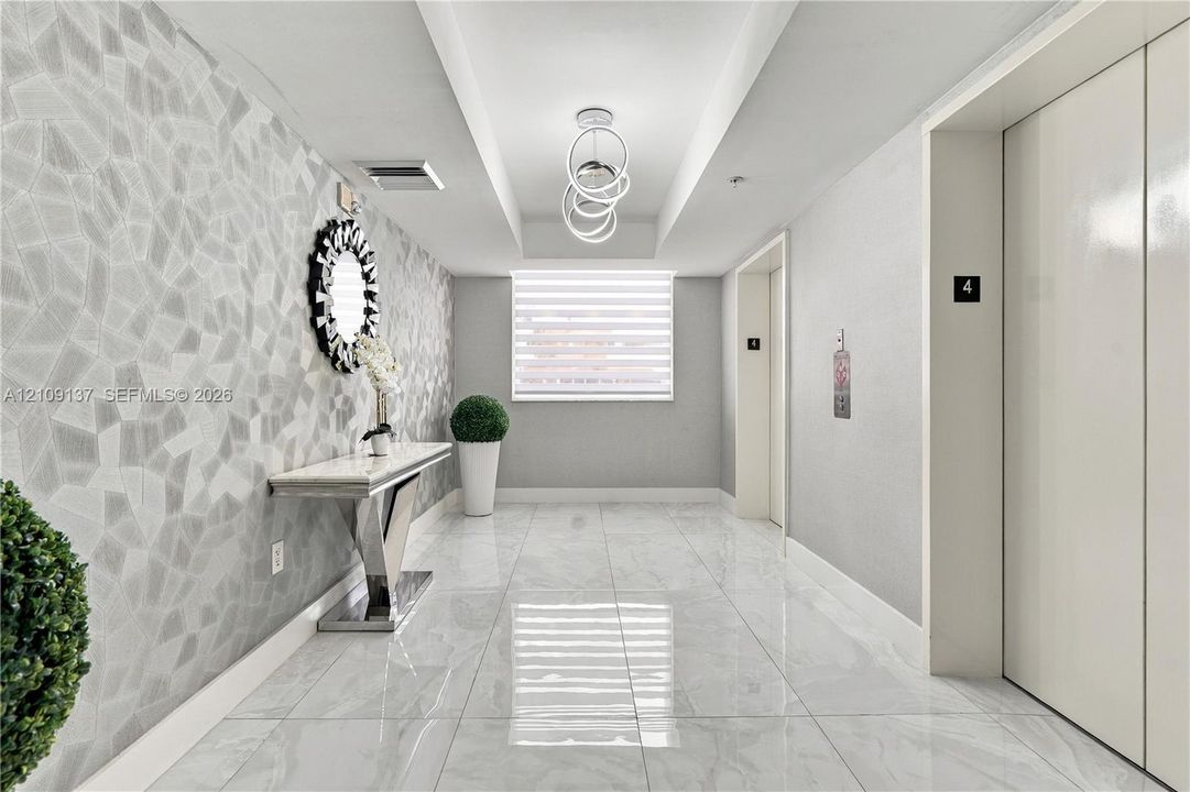 Entryway featuring large-format polished tile flooring, geometric textured wall covering, recessed ceiling detail, and contemporary ring chandelier