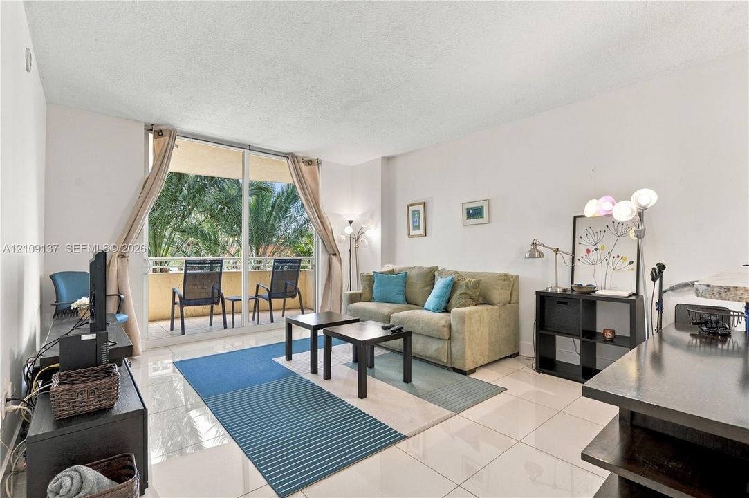 Living space featuring large-format tile flooring, oversized floor-to-ceiling glass sliding doors, and a private balcony