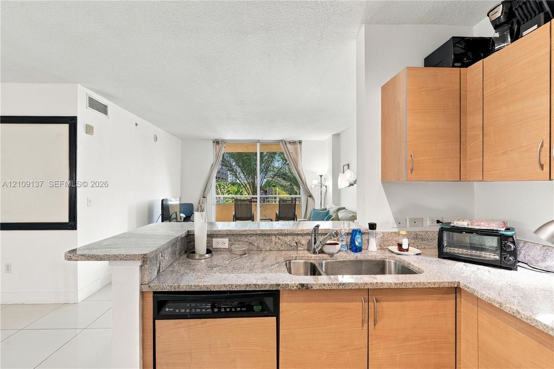 Kitchen featuring natural stone countertops, light wood-finish cabinetry, stainless steel double-basin undermount sink, and integrated dishwasher