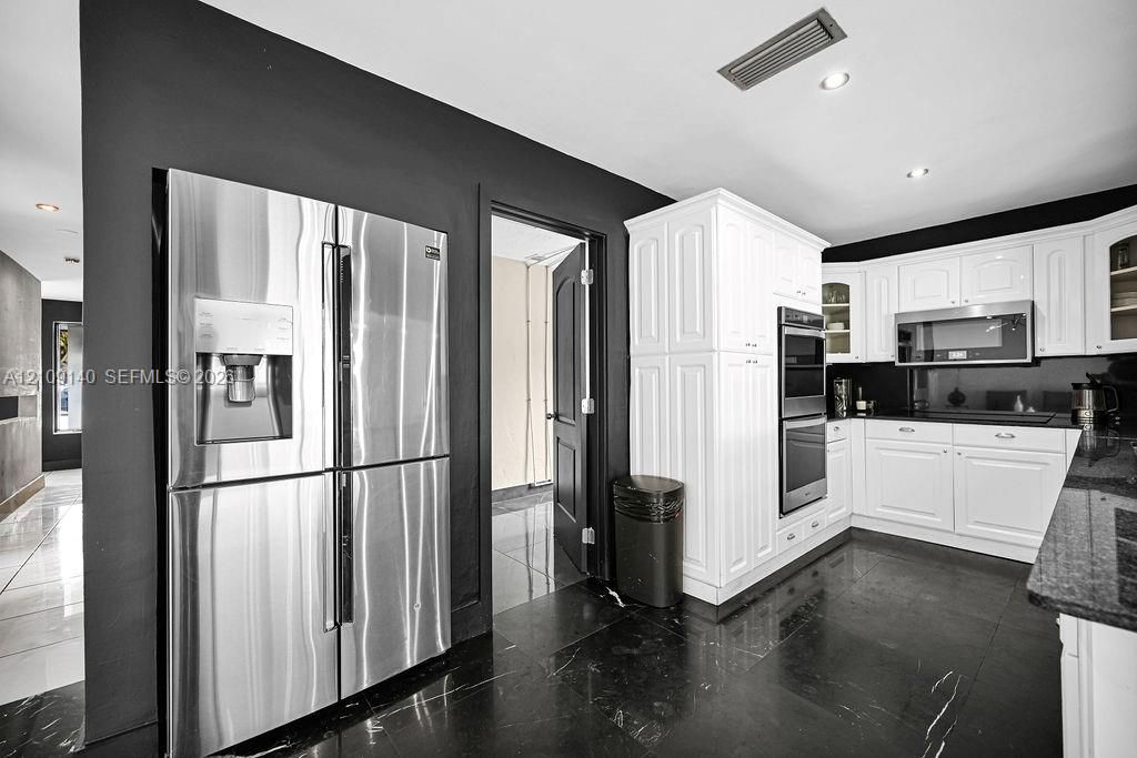 Kitchen featuring white cabinetry, stainless steel double wall ovens, a stainless steel refrigerator, dark stone countertops, and black tile flooring