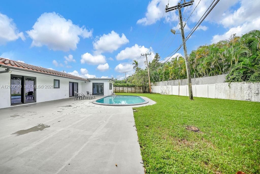 Spacious backyard featuring an in-ground swimming pool, concrete patio, lawn area, and perimeter privacy fencing
