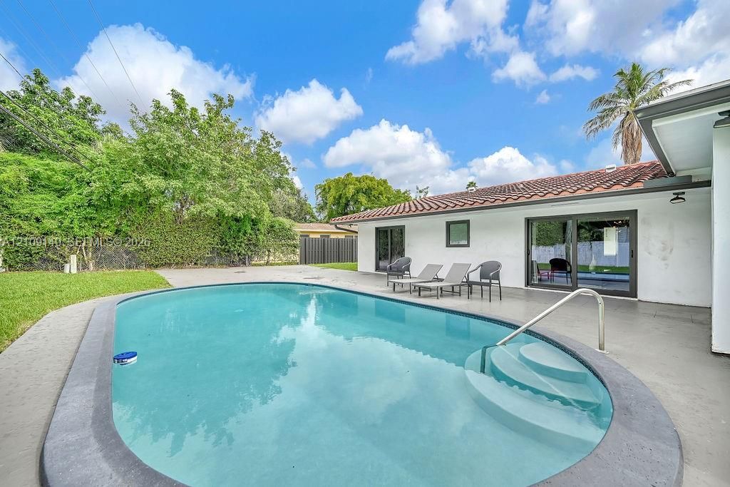 In-ground pool featuring concrete decking and built-in steps, complemented by exterior sliding glass doors and a tile roof