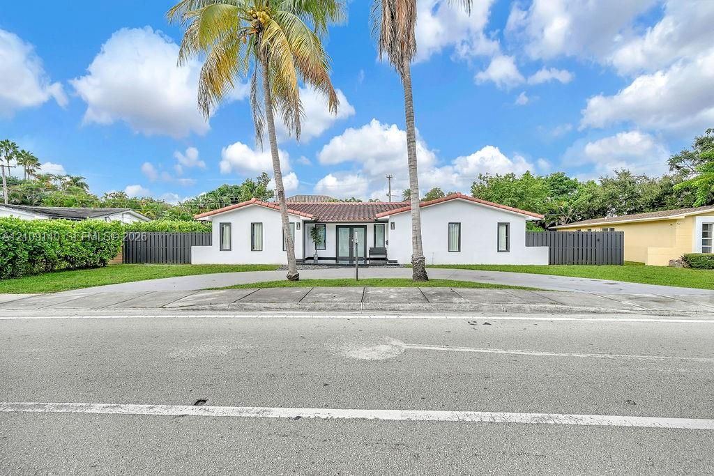 Single-story exterior featuring a white stucco facade, barrel tile roofing, a concrete circular driveway, and dark vertical privacy fencing