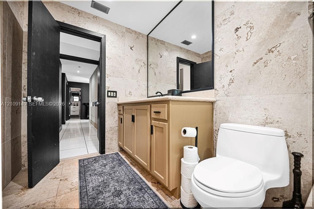 Bathroom featuring floor-to-ceiling stone wall tiling, a vanity with stone-surfaced countertop, a framed wall mirror, and matte black hardware