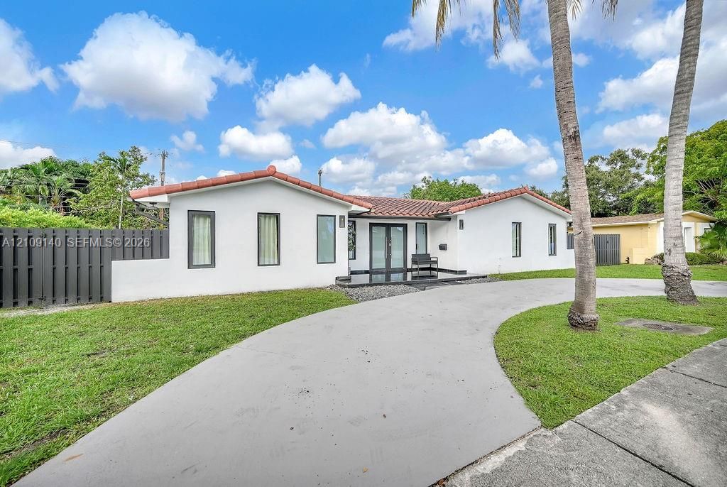 Single-story exterior featuring white stucco siding, a terracotta tile roof, a circular concrete driveway, and dual glass entry doors