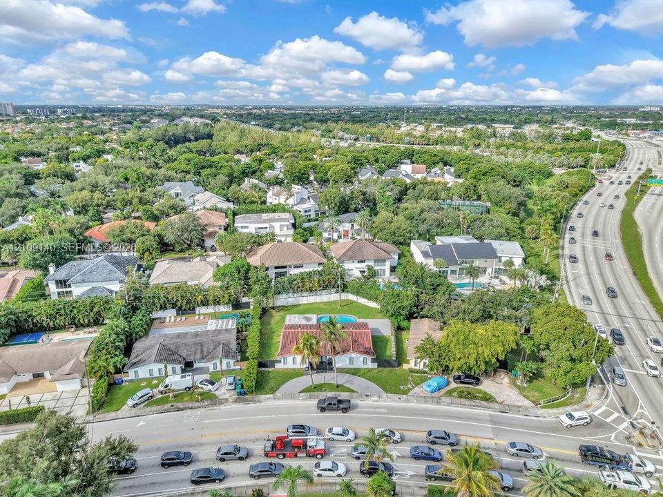 Aerial perspective of a property featuring a multi-pitched roof, a semi-circular paved driveway, mature palm trees, and an in-ground swimming pool