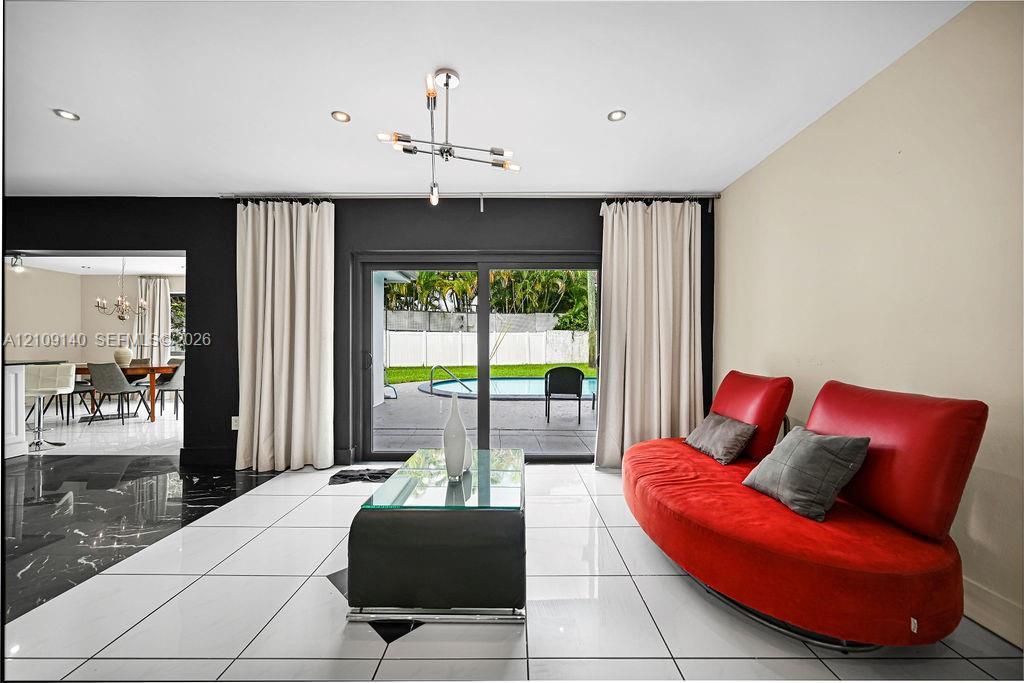 Large-format white tile flooring with contrasting black stone tile inlay, multi-arm modern light fixture, recessed ceiling lighting, and sliding glass doors opening to a backyard swimming pool