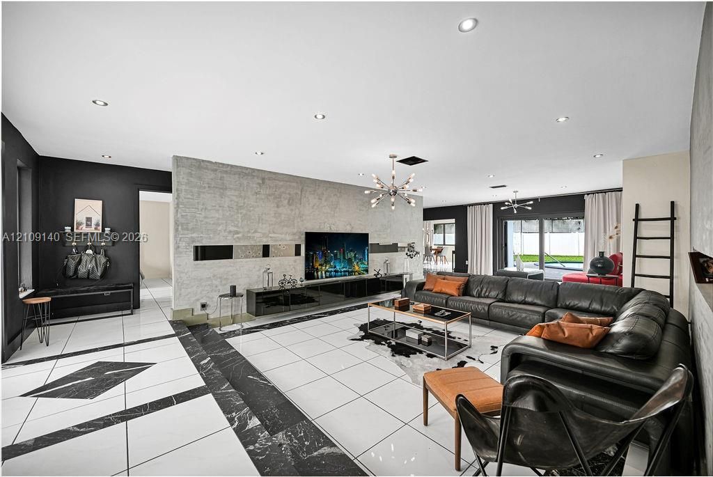 Large living space featuring high-contrast white and black tile flooring, a prominent textured accent wall with built-in cabinetry, recessed lighting, and contemporary chandelier fixtures