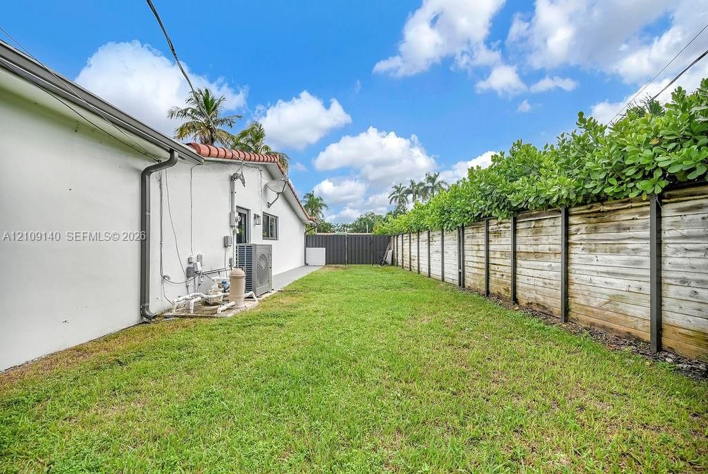 Side yard featuring a grass lawn, horizontal wood-plank perimeter fencing, and mature hedge greenery