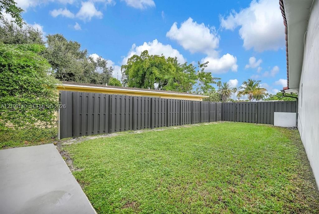 Fenced backyard featuring a manicured lawn, concrete patio, and mature perimeter trees