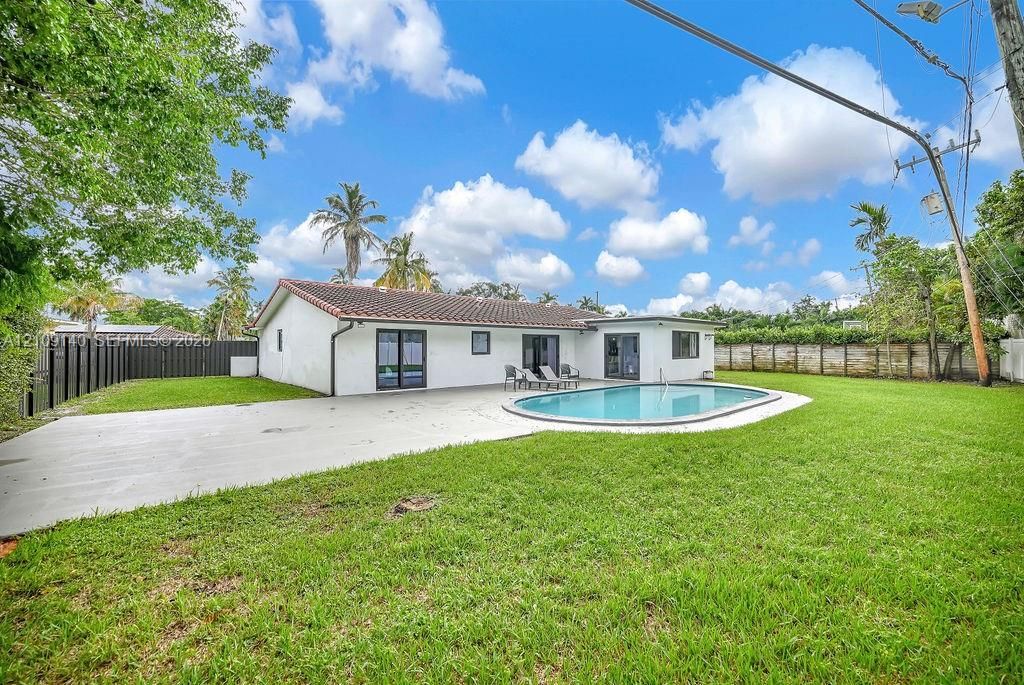 Expansive backyard featuring a curvilinear inground swimming pool, concrete patio, perimeter fencing, and established landscaping