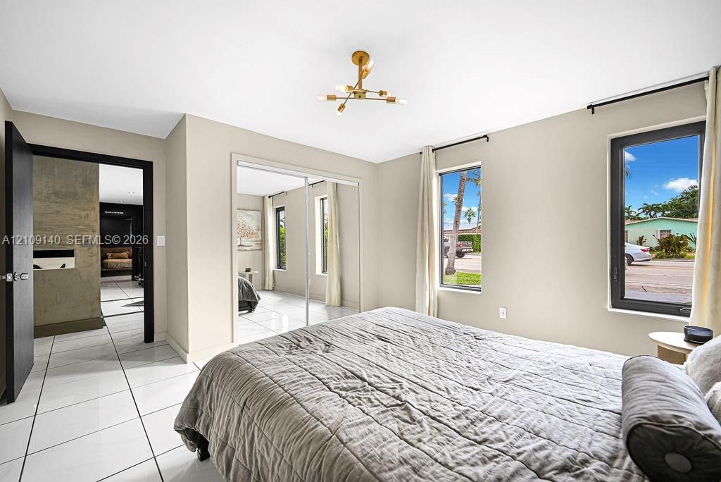 White tile flooring, modern gold-finish multi-arm chandelier, mirrored sliding closet doors, and dark-framed windows