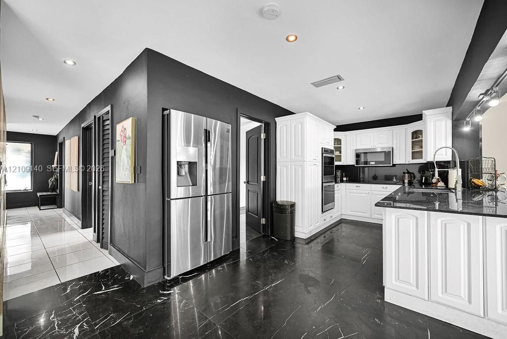 Kitchen featuring white cabinetry with raised-panel detailing, stone-finish countertops, stainless steel appliances, black tile flooring, and recessed ceiling lighting