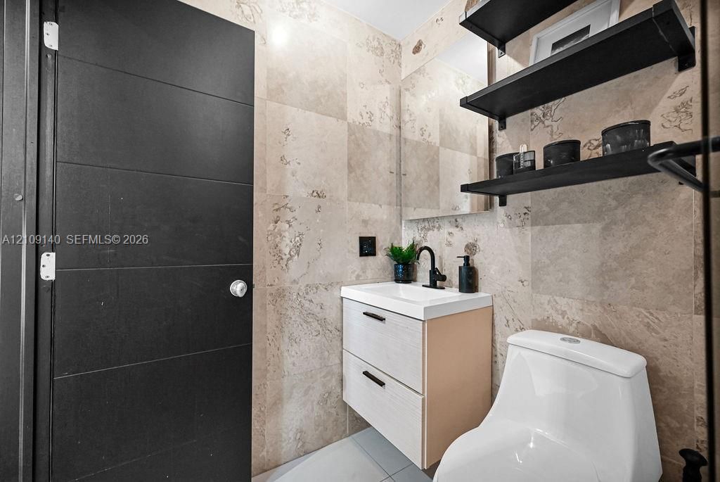 Stone-tiled walls, wall-mounted floating vanity with double-drawer storage, matte black faucet, and matte black open shelving