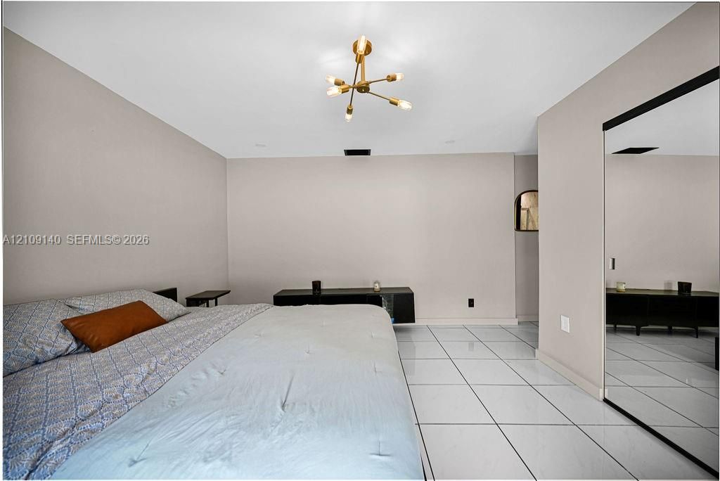 Large-format tile flooring, modern multi-arm brass light fixture, and floor-to-ceiling mirrored closet doors