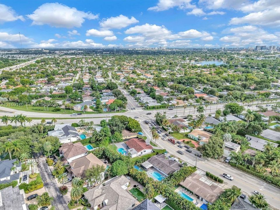 Aerial perspective of a residential neighborhood featuring multi-pitch rooflines, various backyard swimming pools, and mature tree-lined streets