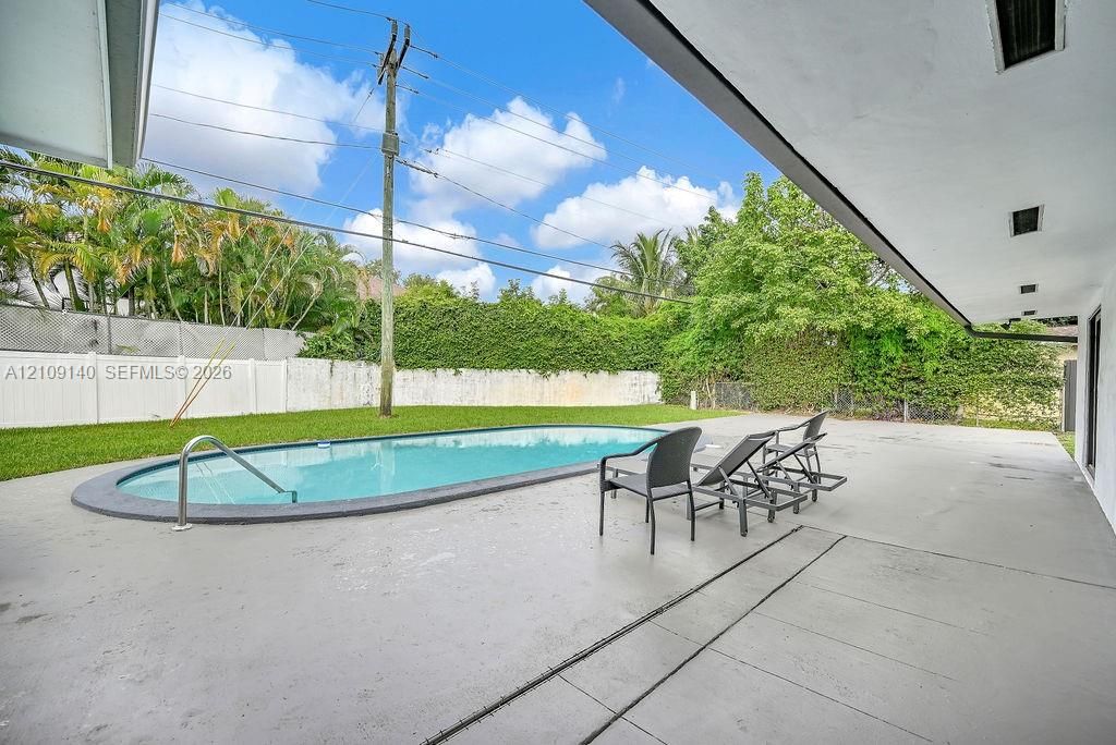 Covered concrete patio with a recessed lighting system, oval swimming pool, and white perimeter privacy fencing