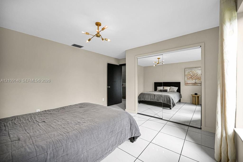 Neutral interior featuring white tile flooring, mirrored closet doors, a multi-arm metallic light fixture, and a solid-core black interior door