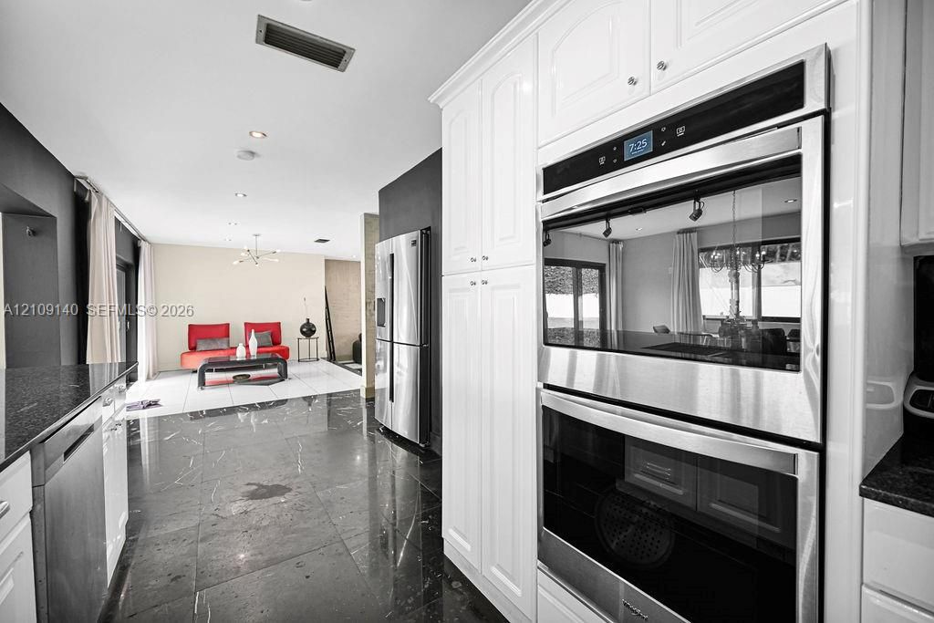 Kitchen featuring white shaker-style cabinetry, stainless steel double wall ovens, stainless steel refrigerator, and dark stone-finish flooring