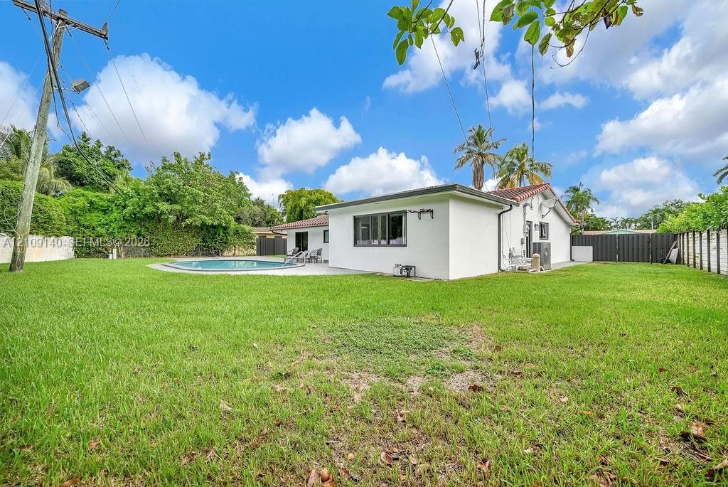 Expansive backyard featuring a manicured lawn, in-ground swimming pool, concrete patio, tiled roof, and privacy fencing