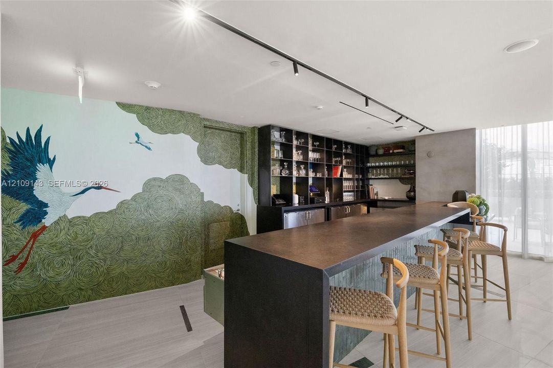 Custom wet bar featuring a solid countertop, integrated shelving, matte black track lighting, and floor-to-ceiling mural