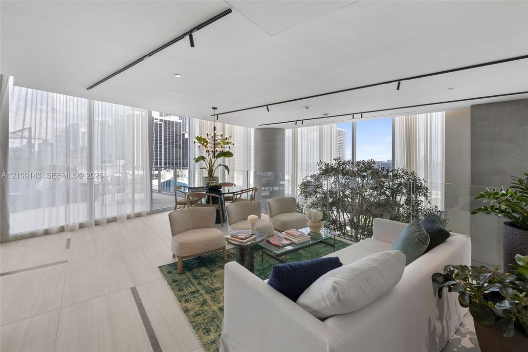 Floor-to-ceiling glass walls, neutral large-format tile flooring, industrial-style track lighting, concrete architectural column, and glass panel railing