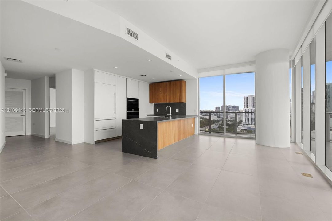 Kitchen featuring flat-panel cabinetry with wood and white finishes, large central island with stone-surface countertop, full-height windows, and tile flooring