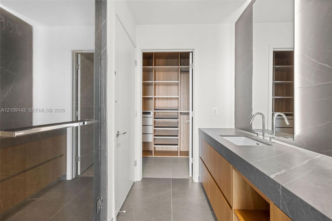 Floating vanity with natural wood-finish cabinetry, stone countertop, integrated rectangular sink, full-height LED-backlit mirror, and custom walk-in closet with built-in shelving