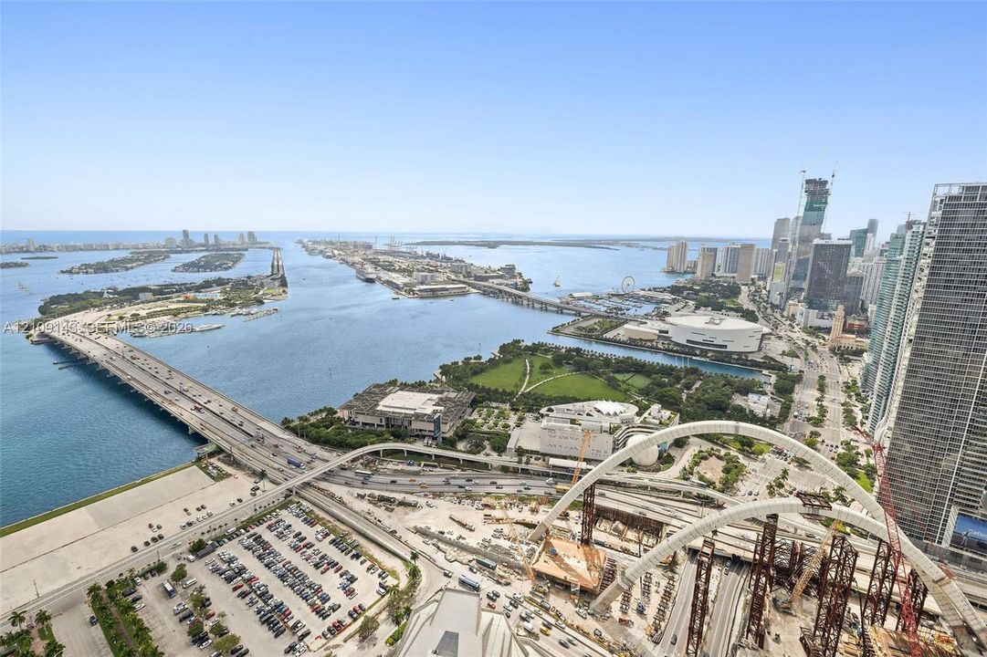 High-rise aerial perspective capturing coastal waterway, city skyline, expansive bridge infrastructure, and urban park space