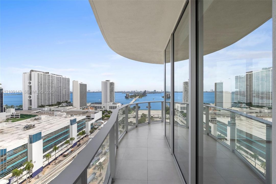 Curved balcony featuring large-format tile flooring and a glass panel railing, framed by floor-to-ceiling glass windows