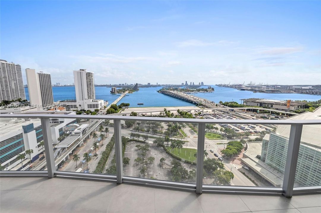 Outdoor balcony with neutral tile flooring and a glass-paneled railing overlooking a cityscape and waterway