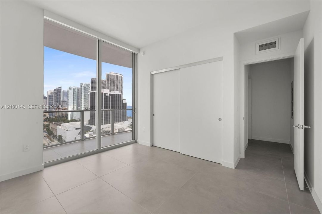 Floor-to-ceiling glass windows, private balcony, large format tile flooring, and built-in sliding door closet