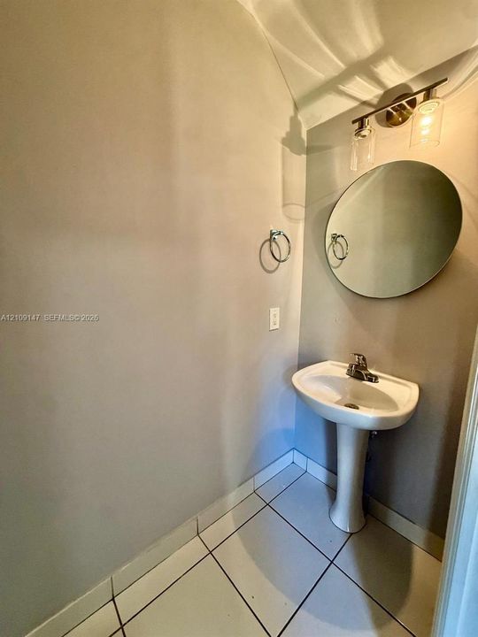 Pedestal sink with a center-set faucet, round frameless mirror, and three-light vanity fixture featuring cylindrical glass shades