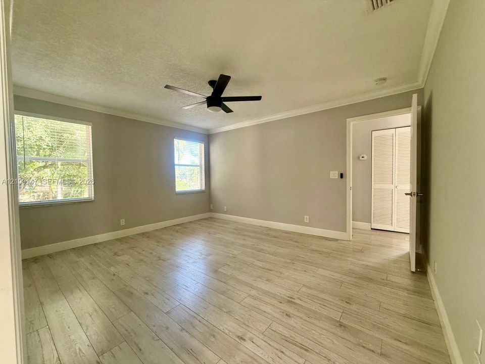 Interior room featuring wood-finish flooring, neutral wall paint, crown molding, a matte black ceiling fan, and louvered-style closet doors