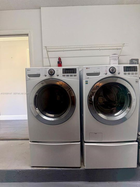 Laundry area featuring two front-loading machines with integrated drawer pedestals and a wall-mounted wire storage shelf