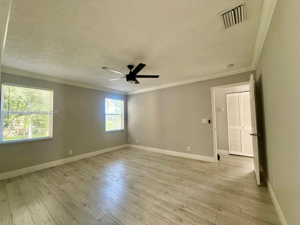 Neutral-toned interior featuring wood-finish flooring, crown molding, multi-pane windows, a ceiling fan, and louvered closet doors