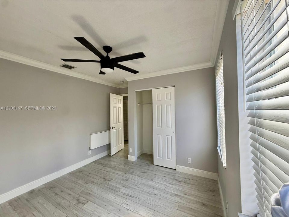 Room featuring wood-finish flooring, crown molding, a multi-blade ceiling fan, and a closet with a six-panel door