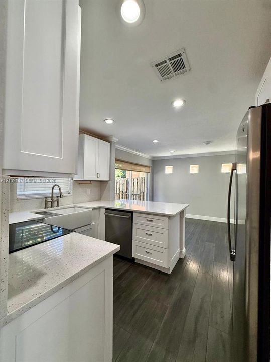Kitchen featuring white shaker-style cabinetry, solid-surface countertops, a farmhouse-style sink, stainless steel appliances, and wood-finish flooring